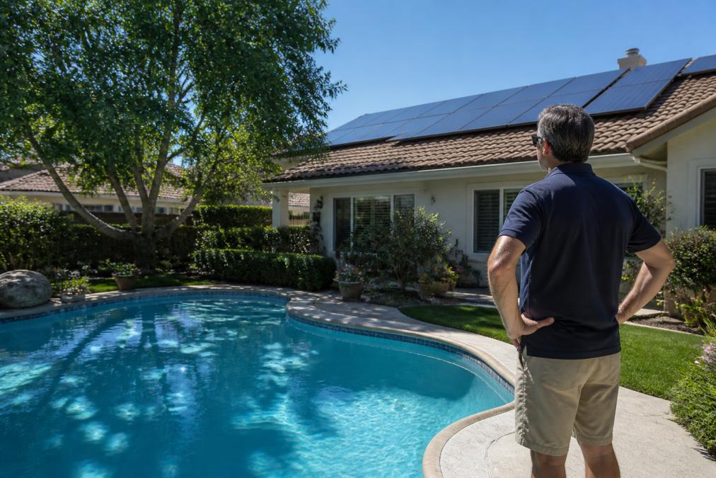 Homeowner observing roof solar panels and shaded pool water affecting pool heater efficiency