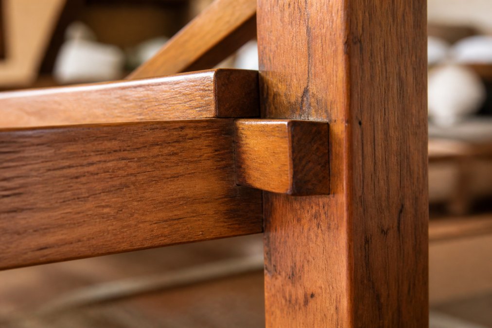 Close-up of solid hardwood furniture frame showing quality joinery details, wood grain texture, and natural patina on exposed wooden joints in warm studio lighting