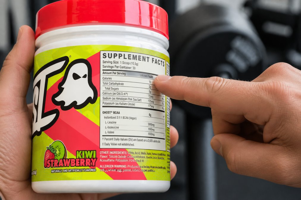 Close-up of a supplement bottle label with someone's hand pointing to the supplement facts panel, showing clear ingredient listings and dosage information in natural lighting
