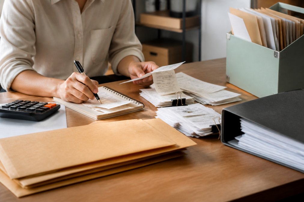 Professional organizing receipts and invoices at desk with laptop, filing system, calculator, and organized folders for business expense documentation