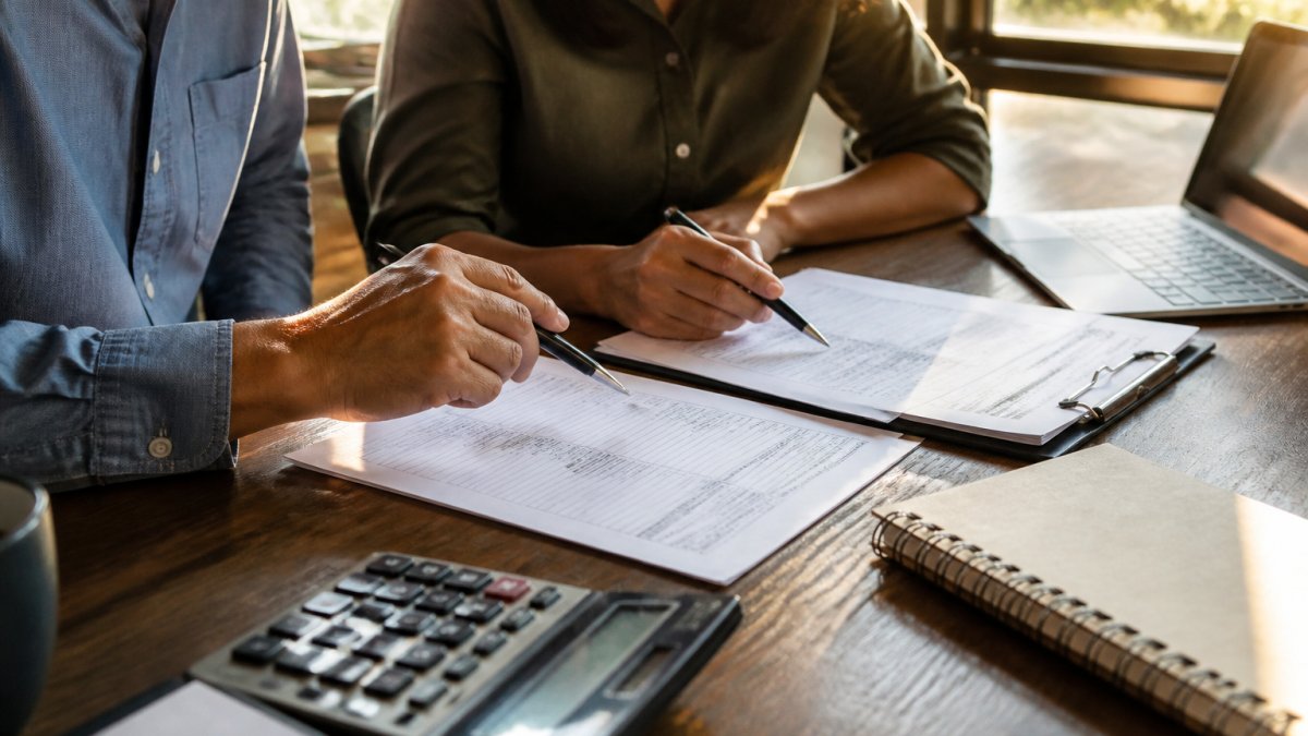 A small business owner and an accountant reviewing a worker classification checklist at a wooden desk with a laptop and tax forms, natural window light, focused discussion