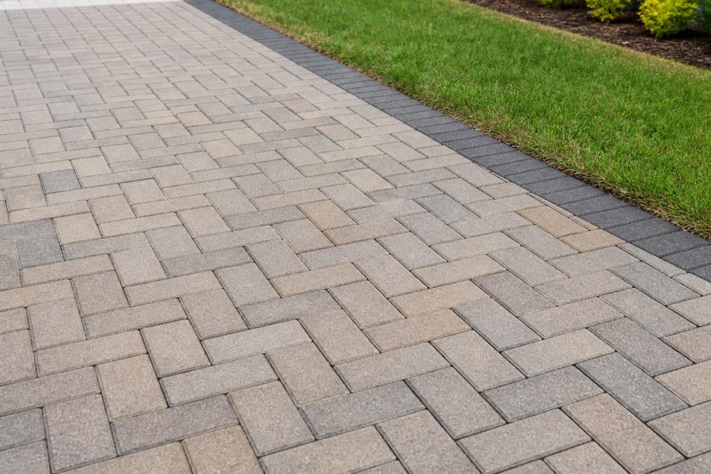 Close-up of a freshly cleaned block paving driveway with crisp, well-defined joint lines, a neat green lawn border running along the edge, photographed in bright overcast daylight that shows the clean surface texture clearly