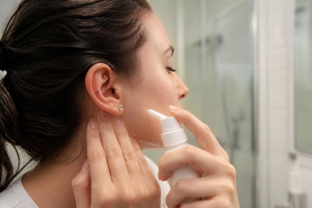 Close-up of a person using a sterile saline spray on a new ear piercing, with clean hands and a calm, bright bathroom setting