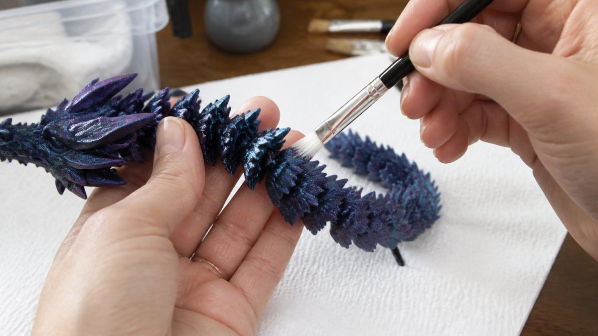 Close-up of hands using a soft-bristled brush to gently clean dust from the articulated joints of a small resin dragon figurine on a clean workspace