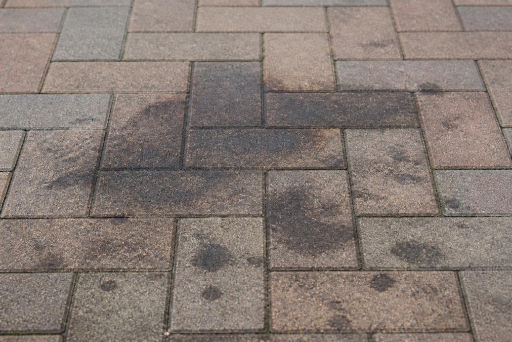Close-up of dark oil stains on block paving surface showing discolouration and texture variation before cleaning treatment