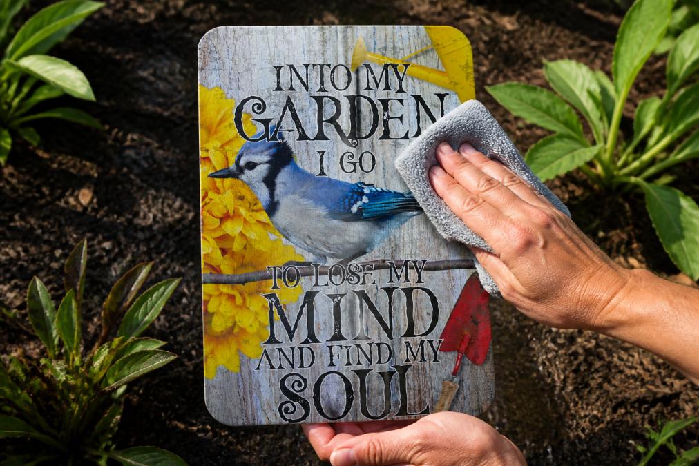 Hands using a soft microfiber cloth to buff and dry an outdoor aluminum garden sign, showing the transformation from wet surface to restored shine with natural sunlight reflecting off the metal