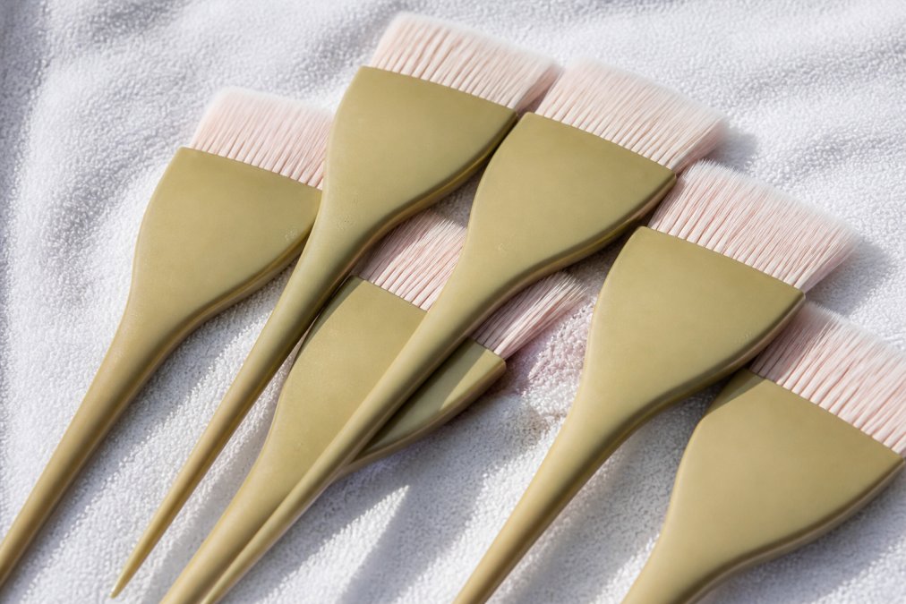 Flat lay of multiple professional hair tint brushes with feathered tips laid out on a clean white salon towel, showing bristle detail and ferrule construction under bright studio lighting