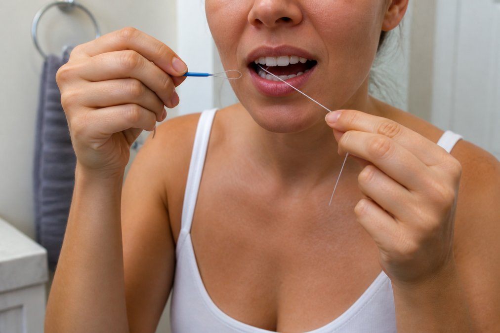 Person using a floss threader to clean underneath a dental bridge in a bright bathroom setting