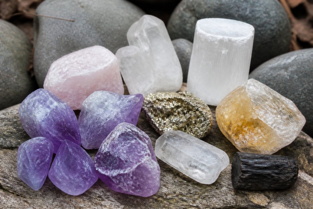 Close-up of various raw crystals and gemstones displayed on a natural surface, showing different colors and textures of materials like amethyst, citrine, and selenite