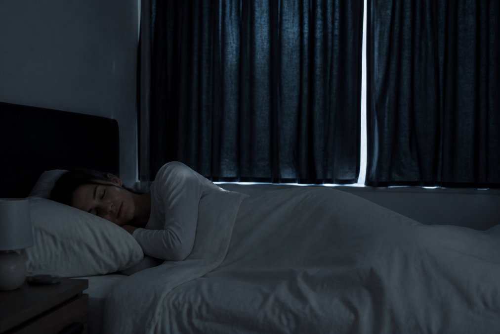 Person sleeping peacefully in a dark, quiet bedroom to help you learn how to clear brain fog through restorative sleep.