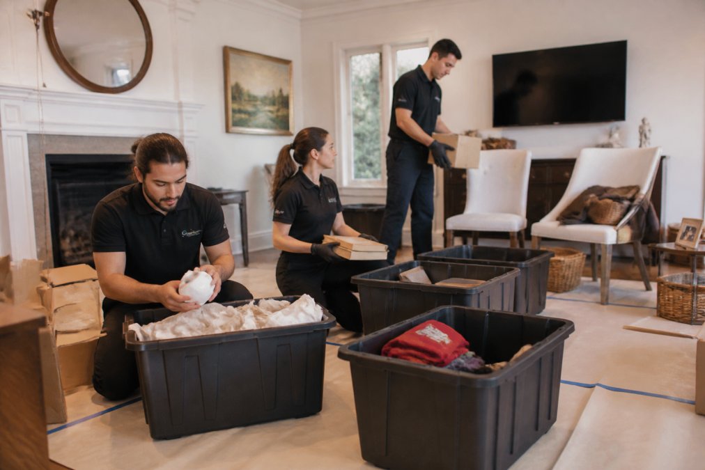 Professional estate cleanout team sorting household items into organized piles labeled keep, donate, recycle, and discard in a residential living room with protective floor coverings and organized workspace