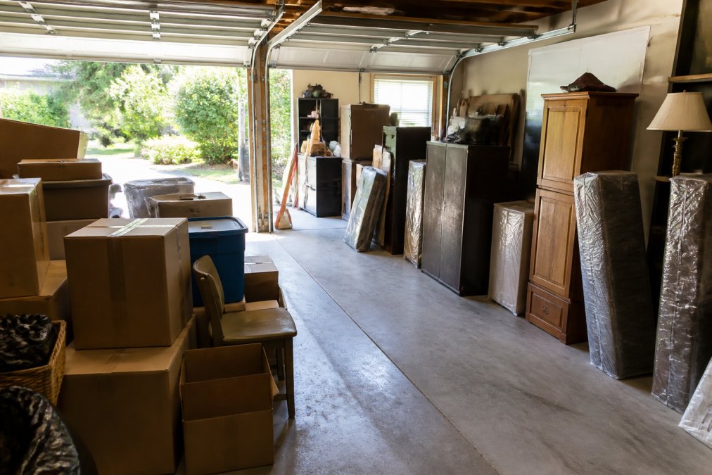 Garage staging area with labeled boxes, furniture stacked neatly, and clear pathways marked for removal crew access, with natural light from garage doors