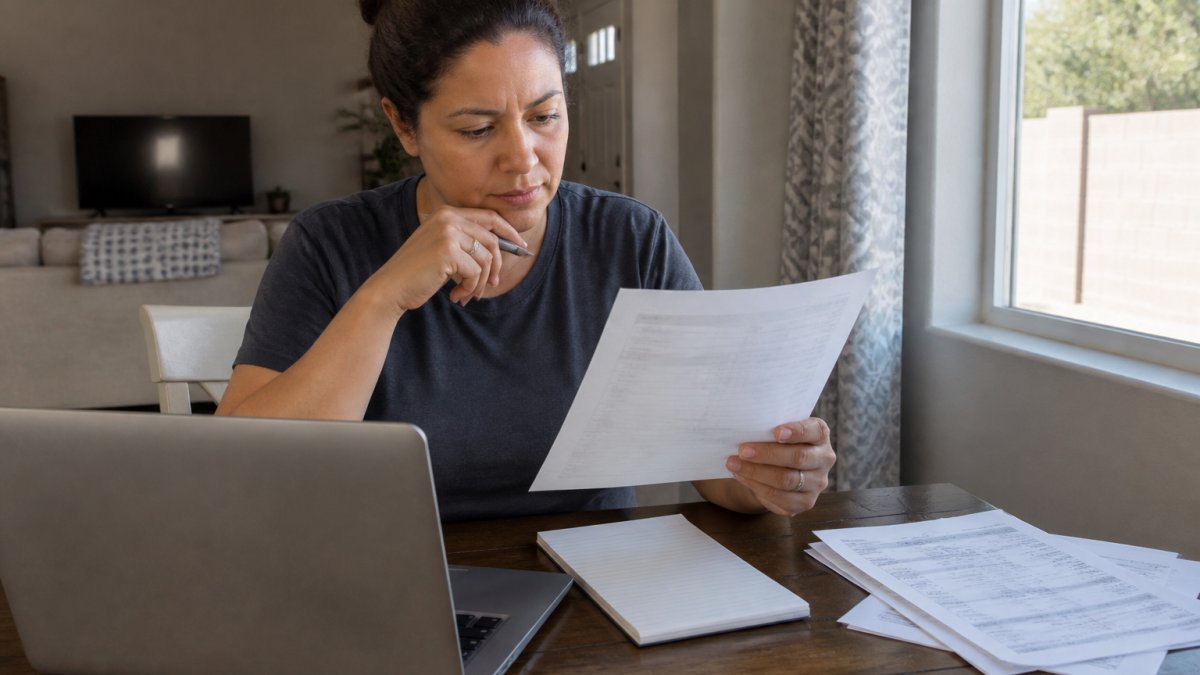 Parent sitting at a table with a laptop and printed checklist, comparing bounce house rental quotes with a notepad and pen nearby