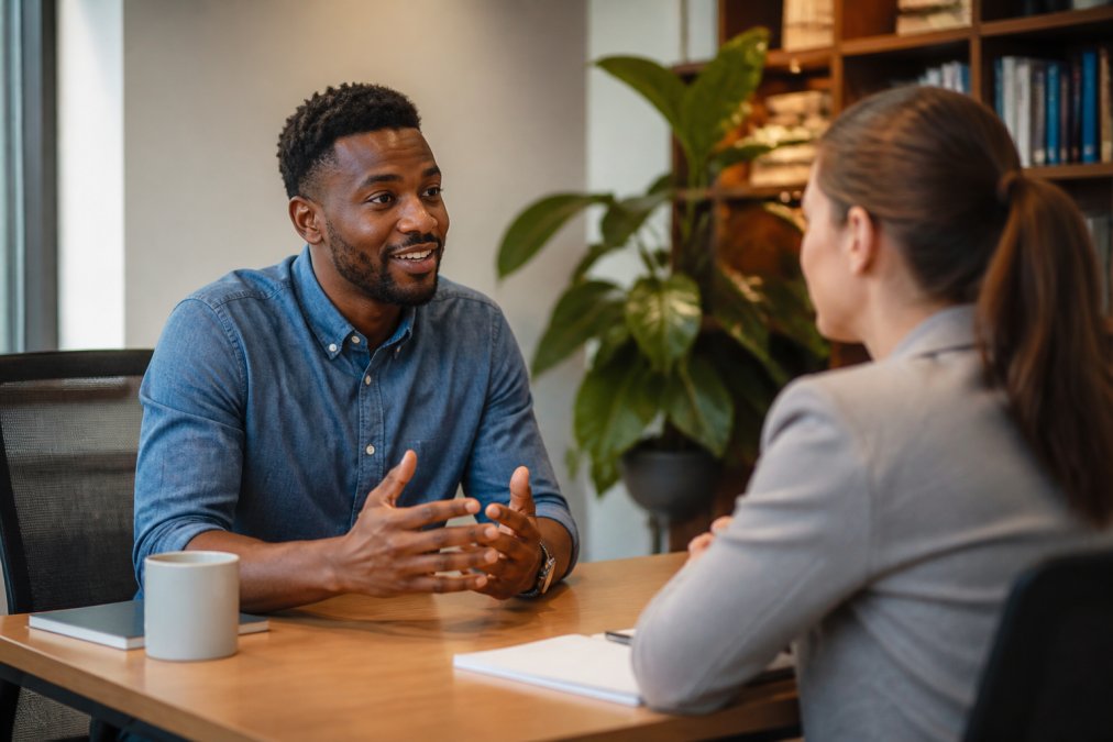 Manager and employee sitting across from each other in a quiet office setting, having a focused one-on-one conversation with open body language and genuine engagement
