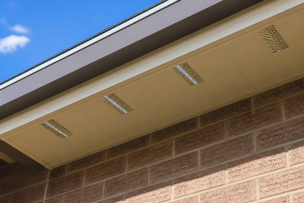 Close-up view of soffit vents along residential roof overhang showing proper spacing and airflow openings, with clear daylight visible through ventilation channels