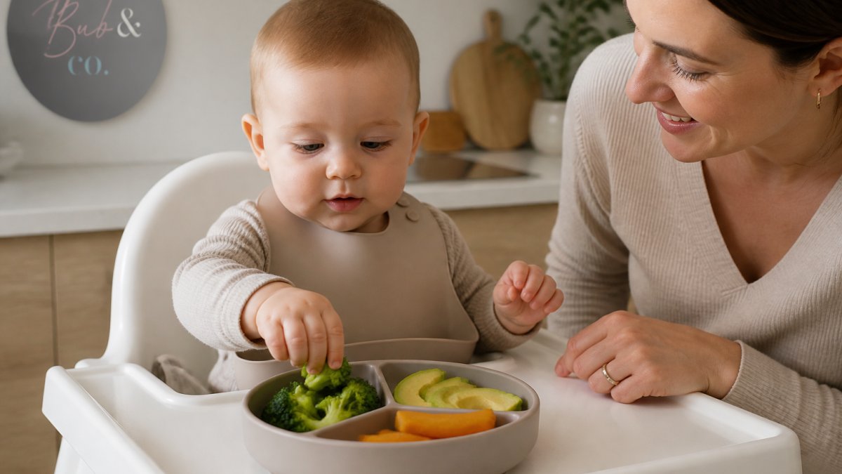 Parent helping baby reach for steamed broccoli and avocado on a suction plate in a sunlit home kitchen