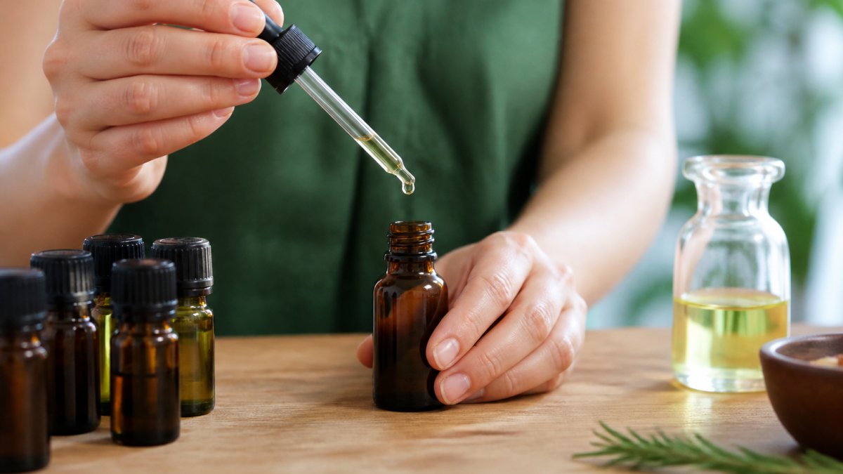 Hands carefully measuring essential oil drops into an amber glass bottle on a wooden table