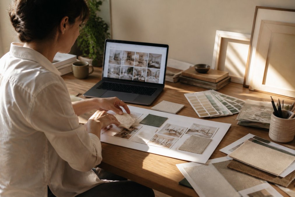 Creative professional using a laptop to learn how to create mood boards with AI tools amidst fabric and color samples.