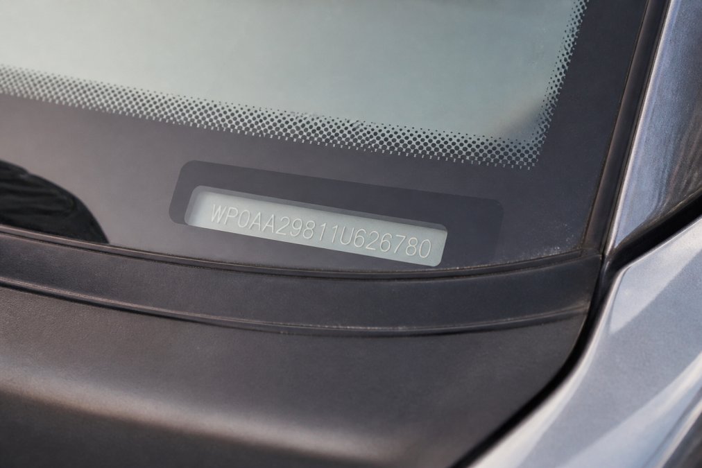 Close-up of Porsche windshield post showing the metal VIN plate with 17-character identification number clearly visible in natural daylight