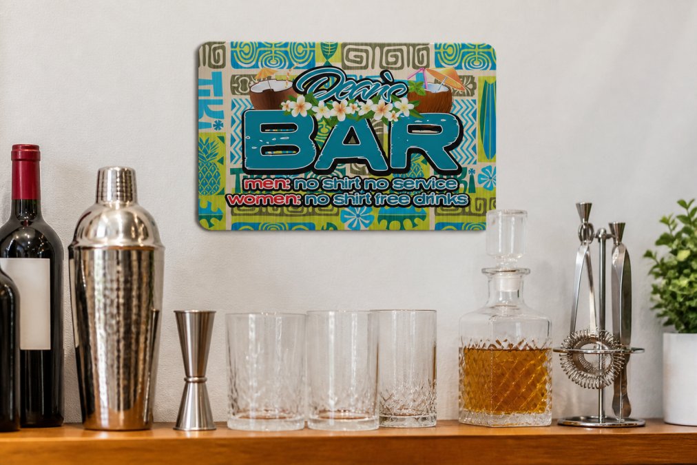 Close-up of a personalized aluminum bar sign mounted on a white wall above a compact home bar setup, showing the sign's vibrant colors and metallic finish, with bottles and glassware visible below