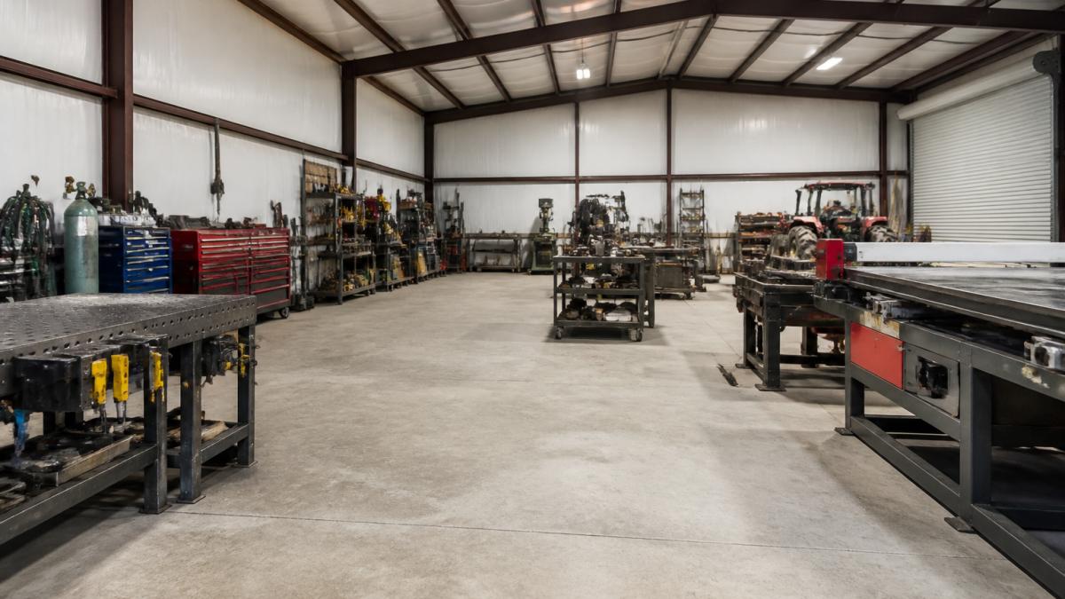 Interior of a functional metal workshop showing organized work zones with tool storage along walls, clear pathways between equipment stations, and proper spacing for equipment movement