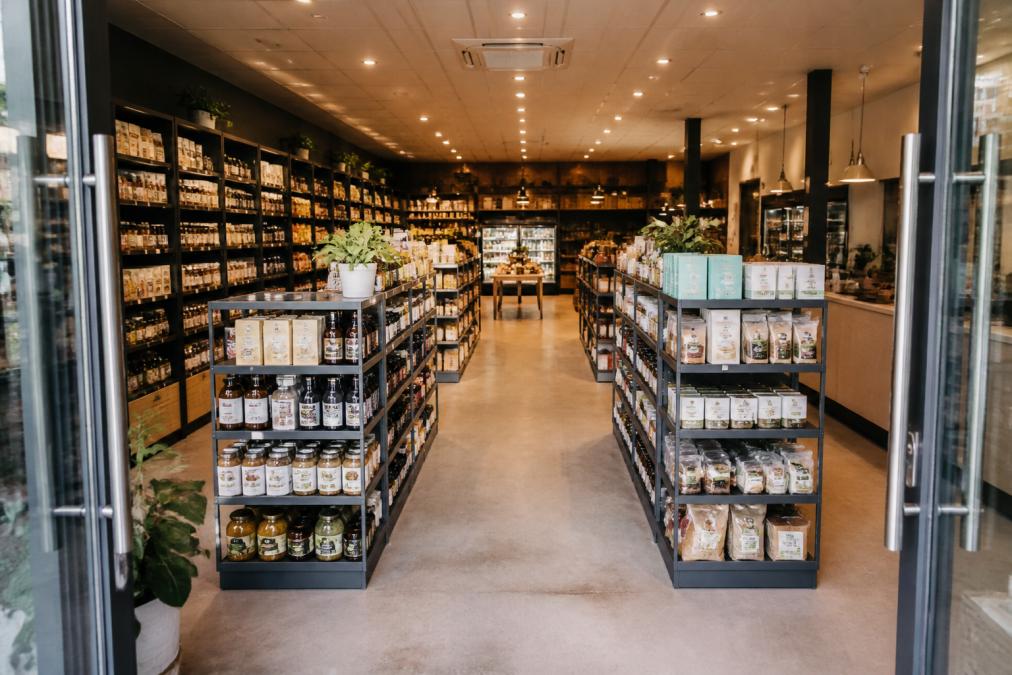 A well-organised independent retail store interior with clear aisles, gondola shelving units, and neatly displayed products on shelves, viewed from the entrance