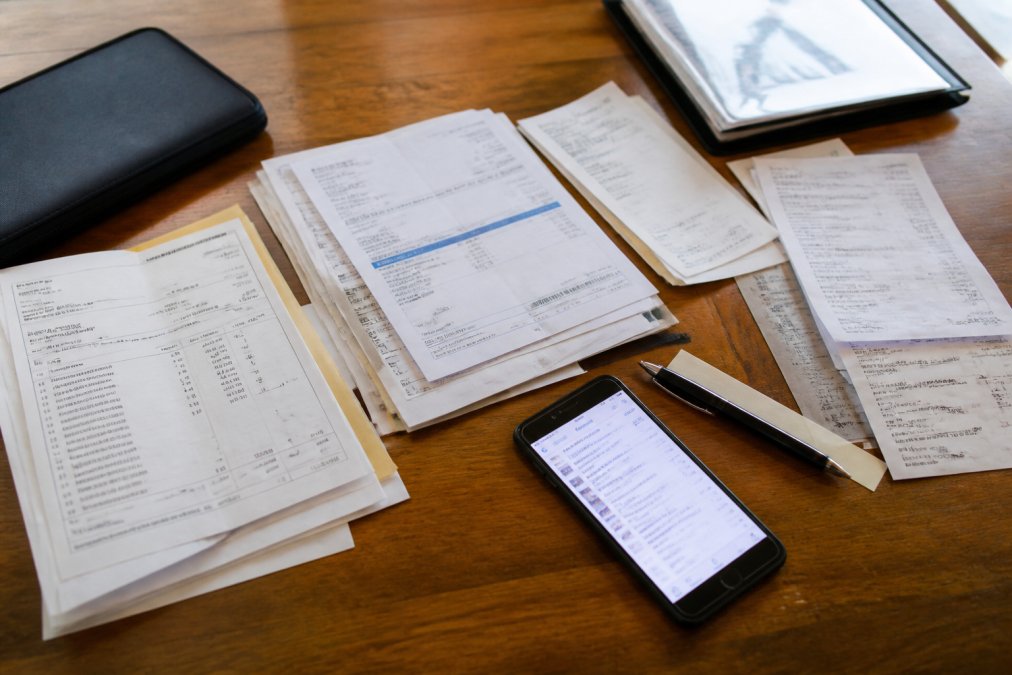 Organized collection of service records, receipts, and invoices spread on a wooden table with a smartphone displaying digital maintenance logs and a pen nearby