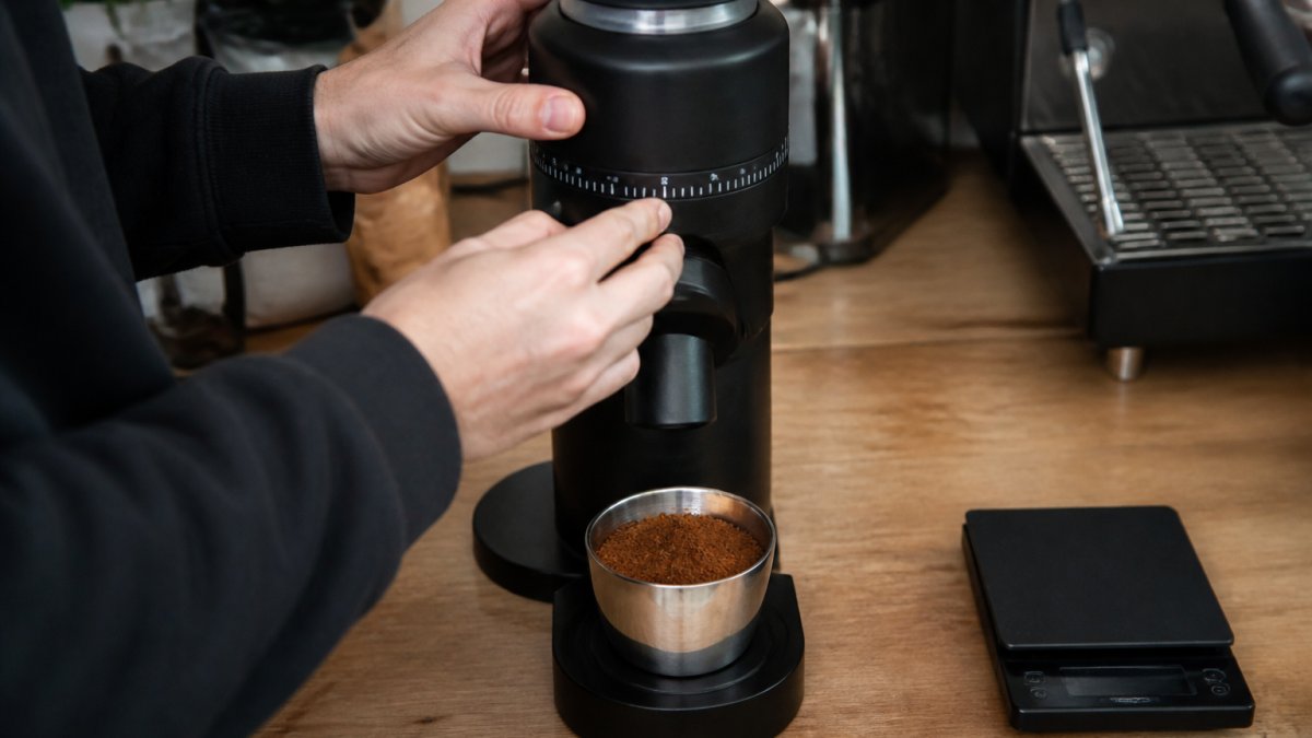 Barista adjusting the grind size on an espresso grinder next to a scale and dosing cup