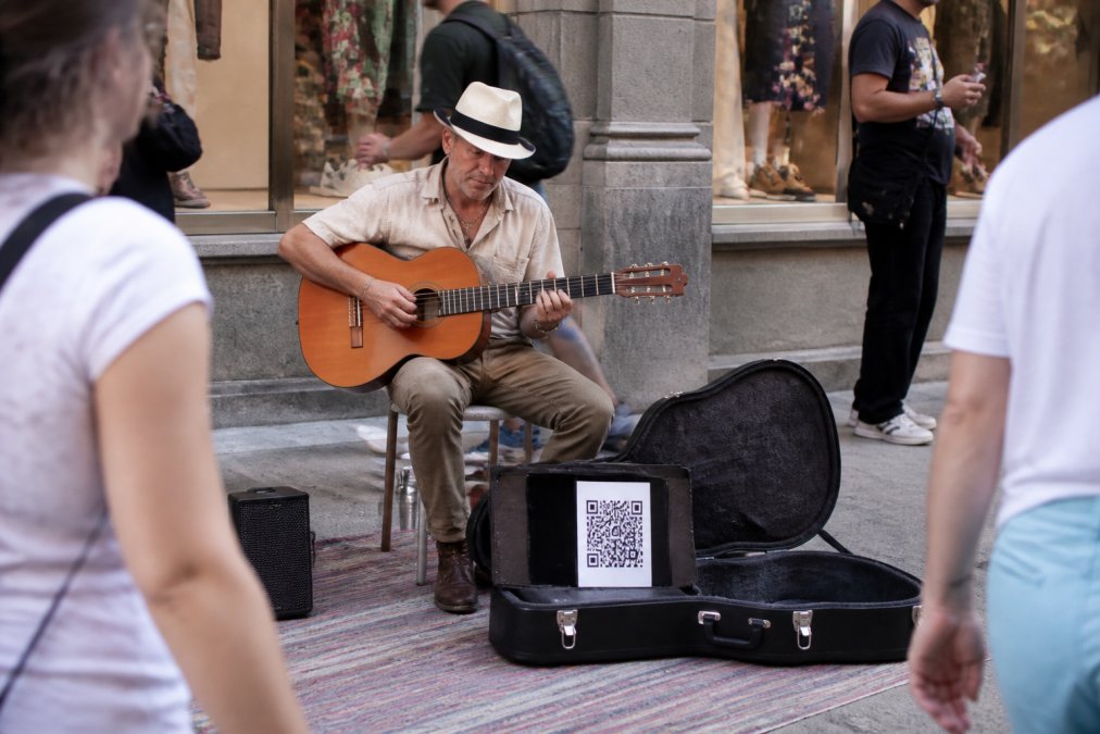 Illustration of a street performer with a QR display beside an instrument case