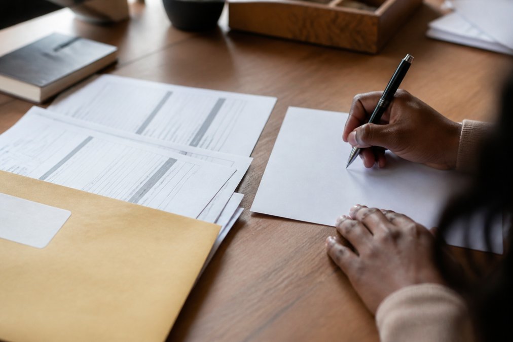Close-up of hands writing a formal dispute letter with pen, with credit report pages and envelope visible on desk, organized and ready to mail
