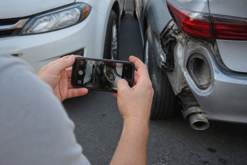 Diagram showing a person using a smartphone to photograph damage at a rideshare accident scene with a timestamp