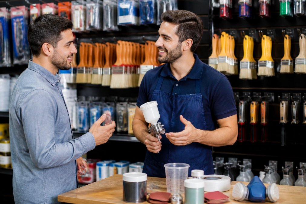 Sales professional in a bright retail setting having an engaged conversation with a customer, both smiling, with product displays visible in the background