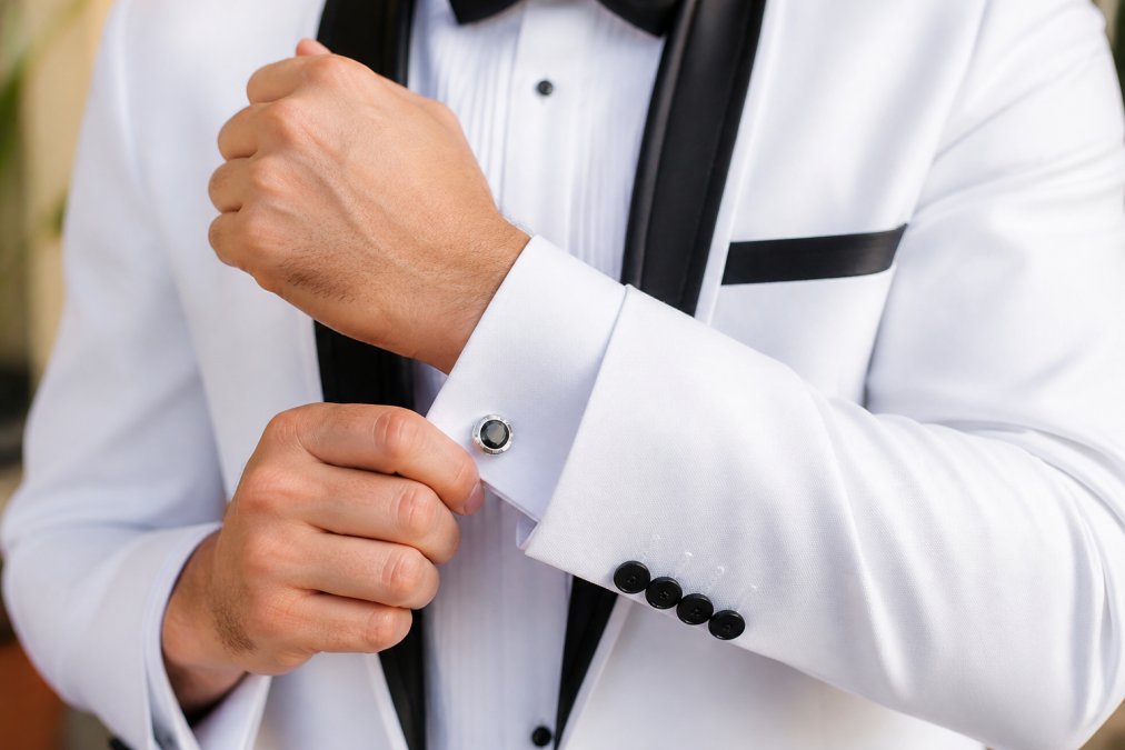 Close-up of formal white dress shirt cuffs showing French cuffs fastened with elegant silver cufflinks, with a coordinated silk pocket square visible in the suit jacket pocket, shot in natural daylight