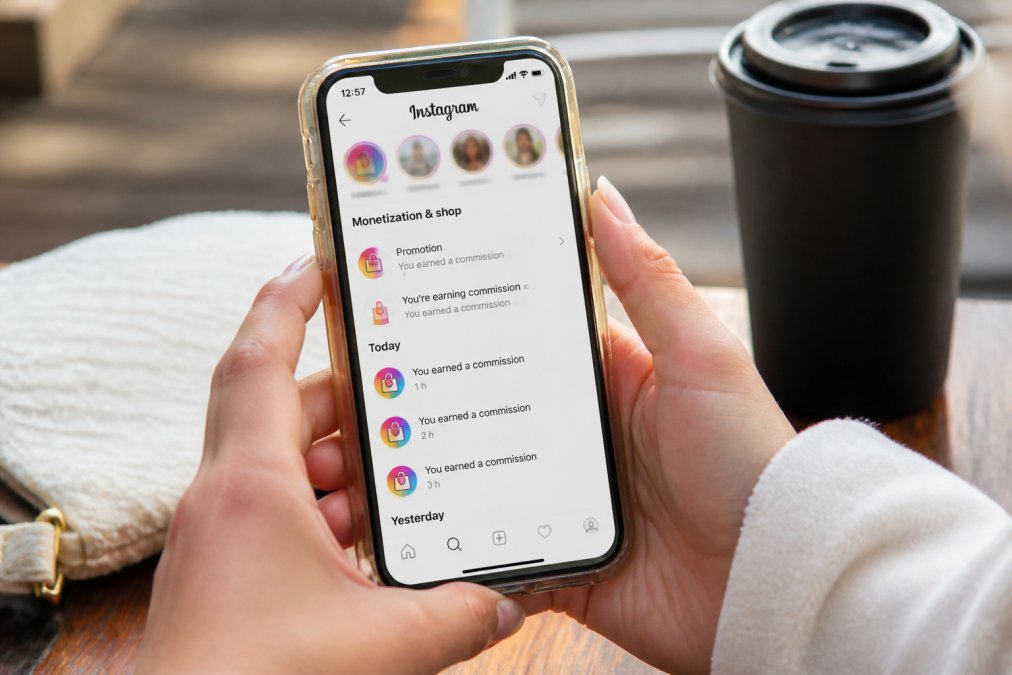 Close-up of hands holding a smartphone displaying Instagram with earnings notifications and commission alerts visible on the screen in bright natural lighting