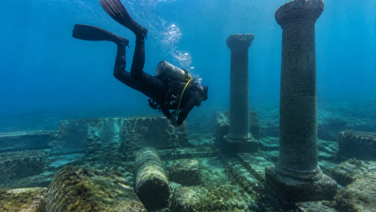 Professional diver descending to explore Portus Julius underwater Roman stone columns and harbor ruins.