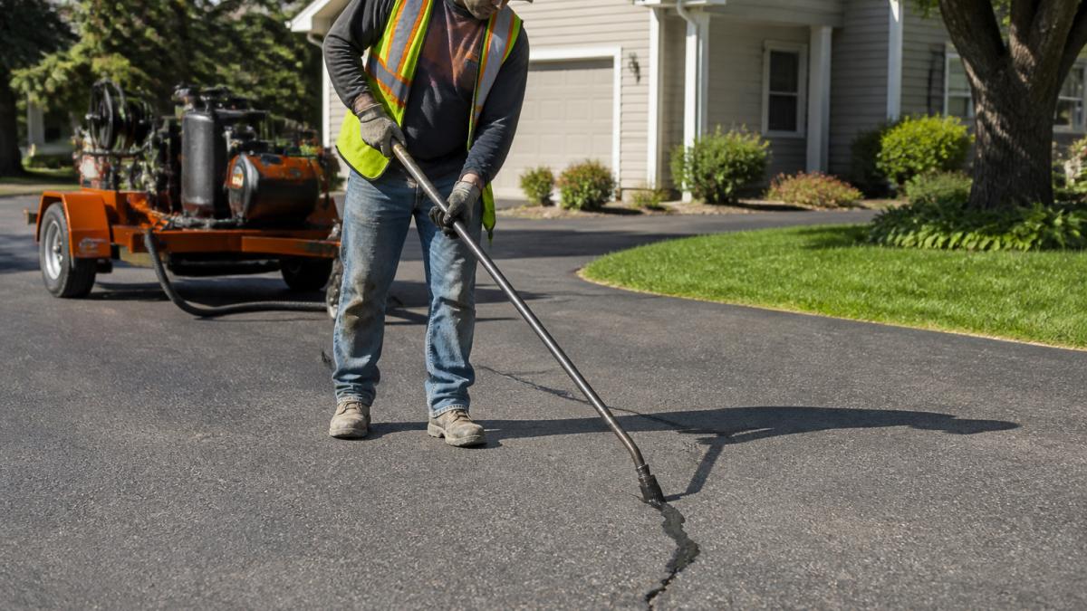 Worker using a sealing wand to repair driveway cracks, showing how to extend the lifespan of asphalt pavement.