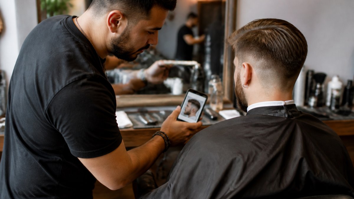 Barber and client reviewing a haircut reference photo on a phone to ensure a consistent barber experience.