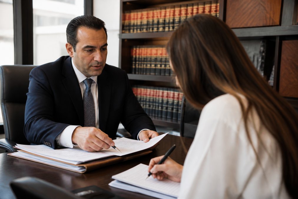 Professional criminal defense attorney and client having a consultation across a desk in a modern law office, with the client taking notes and the attorney explaining case details on documents