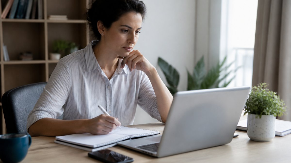 A person sitting at a desk with a laptop, notebook, and phone, researching psychiatric providers in a calm home office setting