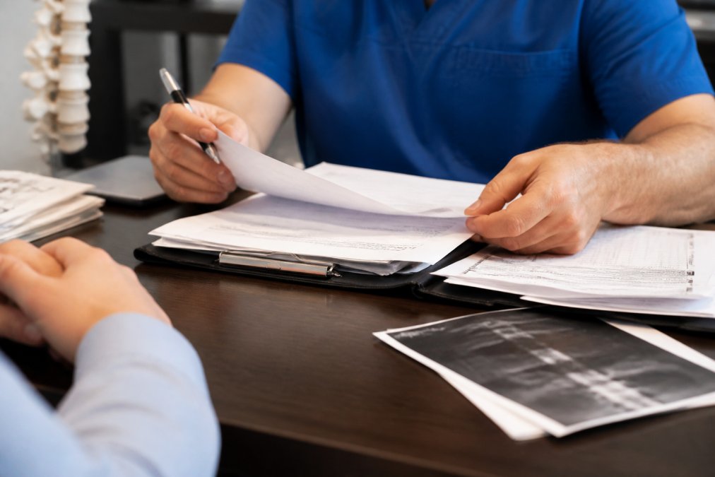 Close-up of hands reviewing medical documents, treatment plans, and insurance paperwork on a desk in a clinical setting