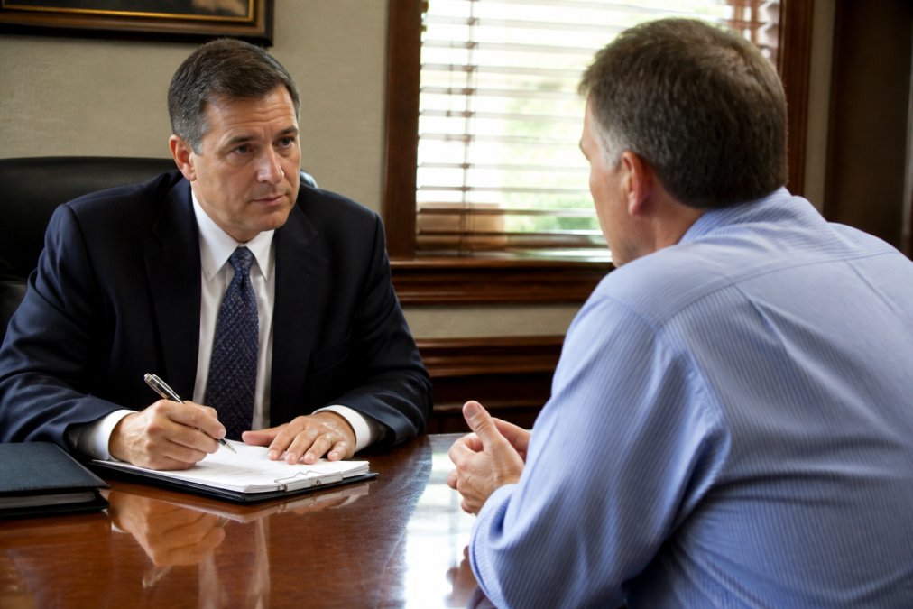 Client and attorney in professional office setting having face-to-face conversation with attorney taking notes, natural office lighting
