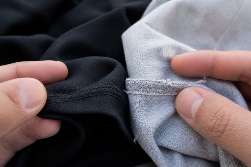 Close-up of hands examining streetwear stitching detail under natural daylight, showing comparison between precise seams and irregular thread work on fabric