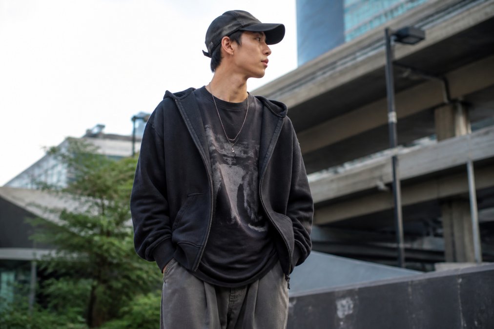 Person wearing layered premium streetwear including oversized hoodie and graphic tee in urban city environment with natural daylight, showcasing authentic construction and fit