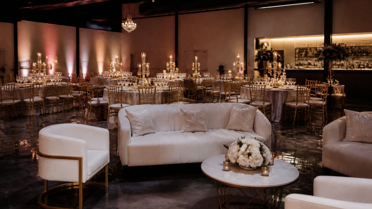Elegantly decorated event space with luxurious lounge seating, ambient uplighting, and formally set tables with centerpieces ready for an upscale celebration