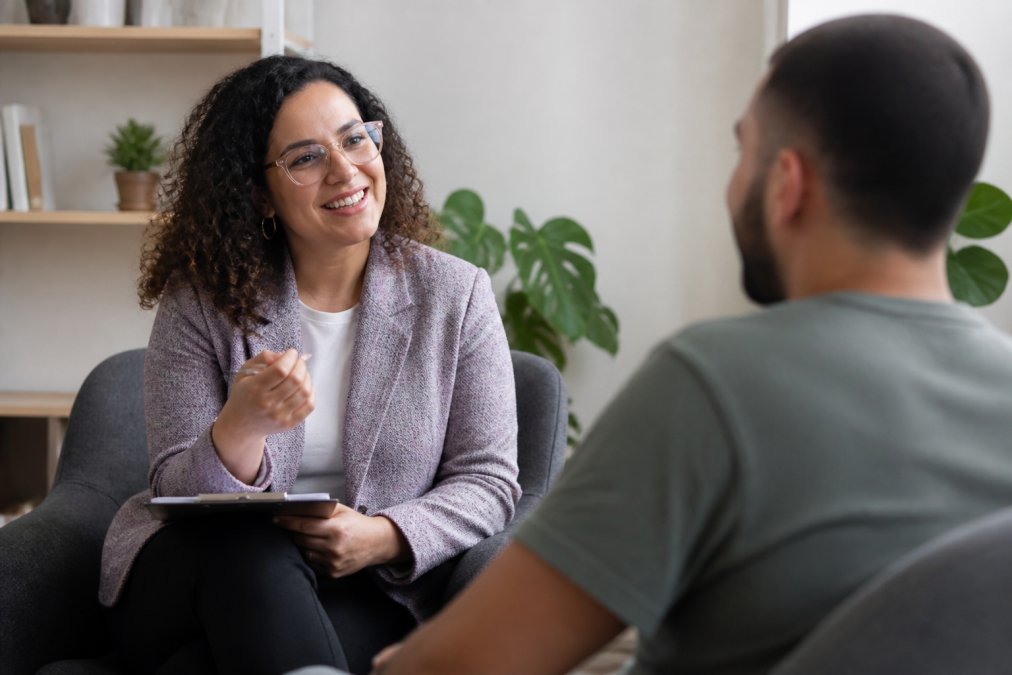Professional therapist having a warm, engaged conversation with client in a modern office with soft natural lighting and welcoming decor, both sitting comfortably
