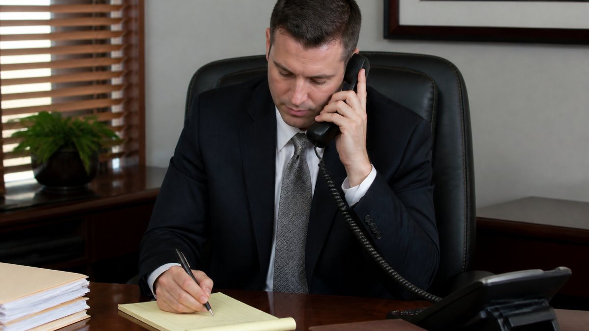 Professional sitting at desk with phone and notepad, making an official inquiry to a government office during business hours