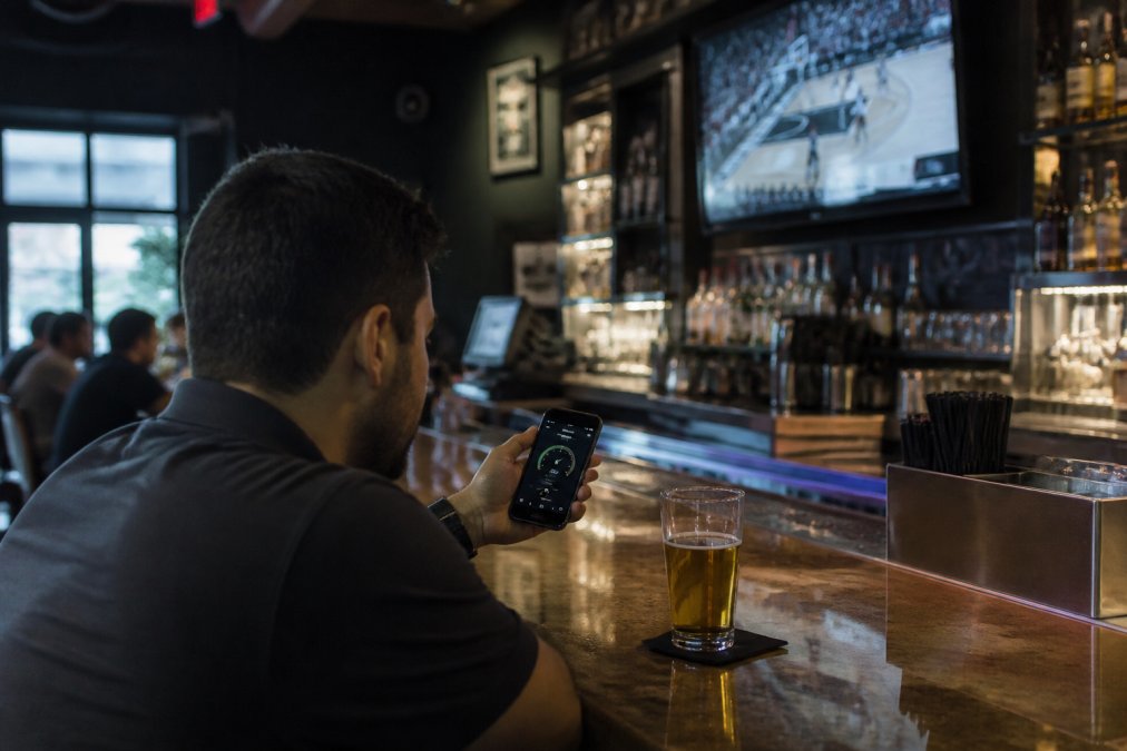 Person checking noise levels on a smartphone inside one of the quiet sports bars while a game plays on TV