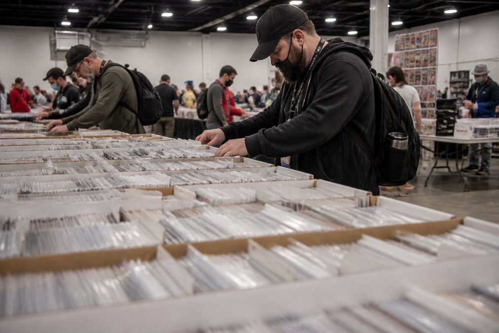 Collector browsing through long boxes of bagged and boarded vintage comics at a crowded comic book convention