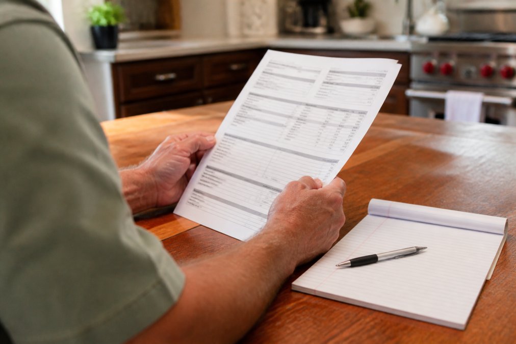 Close-up of hands holding and reviewing a detailed written HVAC estimate document on kitchen table with pen and notepad, natural lighting