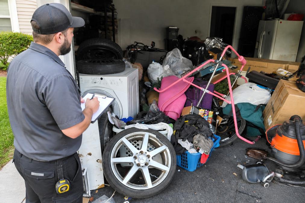 Professional junk removal team taking measurements and notes in a residential garage filled with furniture and boxes